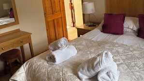 Ein Hotelzimmer mit einem Bett, einem Holztisch, einem Spiegel und einer Tür zu einem weiteren Raum.