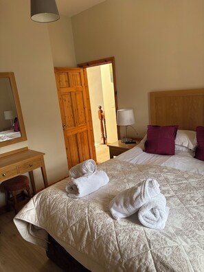 Une chambre dâhĂŽtel avec un lit, un bureau en bois, un miroir et une porte donnant sur une autre piĂšce.
