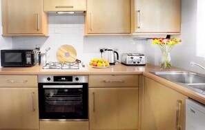 A kitchen with wooden cabinets, a microwave, an oven, a toaster, and a vase with flowers.