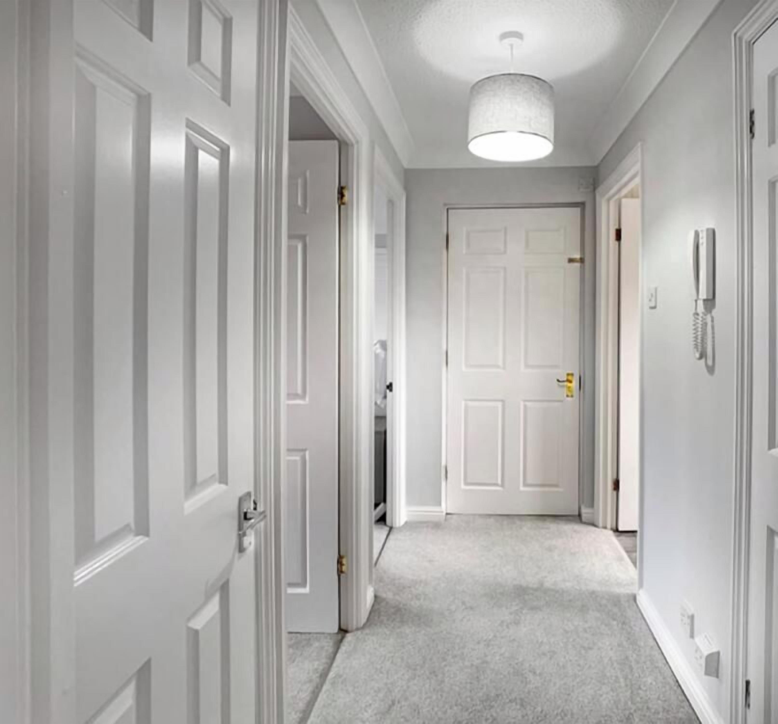 A hallway with white doors, a carpeted floor, and a ceiling light fixture.