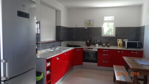 Een kleine keuken met rode kastjes, een inbouwoven, een magnetron en een spoelbak.