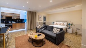 A modern hotel room with a bed, a sofa, a dining table, and a kitchen area in the background. - Newly refurbished, Superior studio Lower Ground (London)