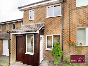A two-story brick house with a front door, a small attached garage, and a mailbox. - Lightwater - 1 Bedroom House - Parking (Lightwater)