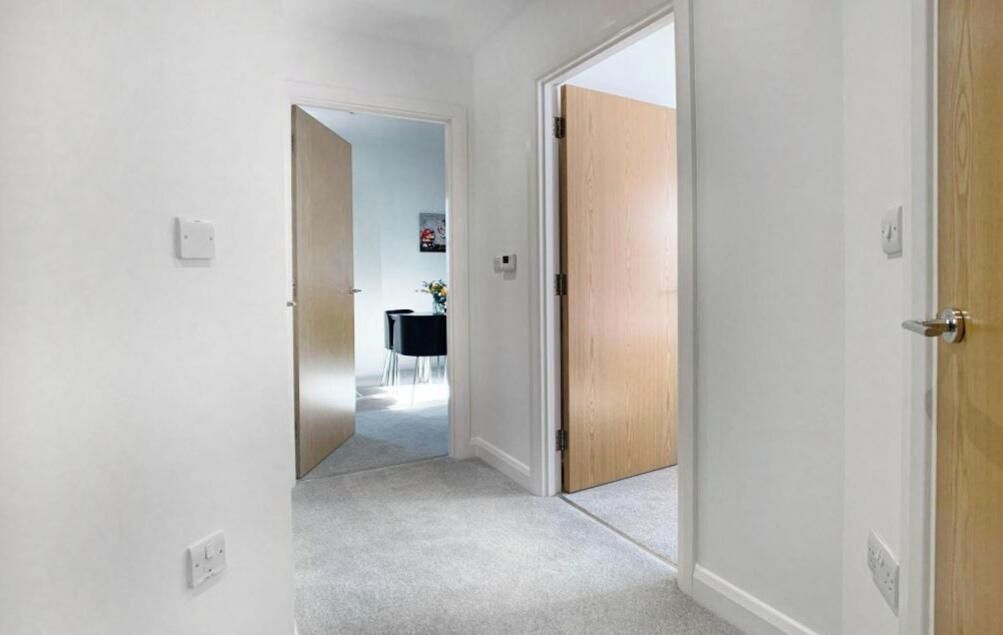 A hallway with carpeted flooring, white walls, and wooden doors.