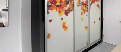 Een kamer met een schuifdeur met herfstblaadjes, een witte deur en een lichtgekleurde vloer.