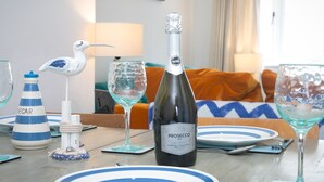 A dining table set with plates, a bottle of Prosecco DOC, and decorative items including a seagull figurine and a striped bottle. - Breeze Cottage  2 bed Beach property - Pass the Keys (Rhosneigr)