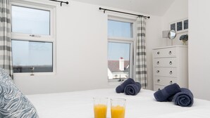 A bedroom with a bed, two windows, a dresser, and a breakfast setup with croissants and orange juice. - Breeze Cottage  2 bed Beach property - Pass the Keys (Rhosneigr)