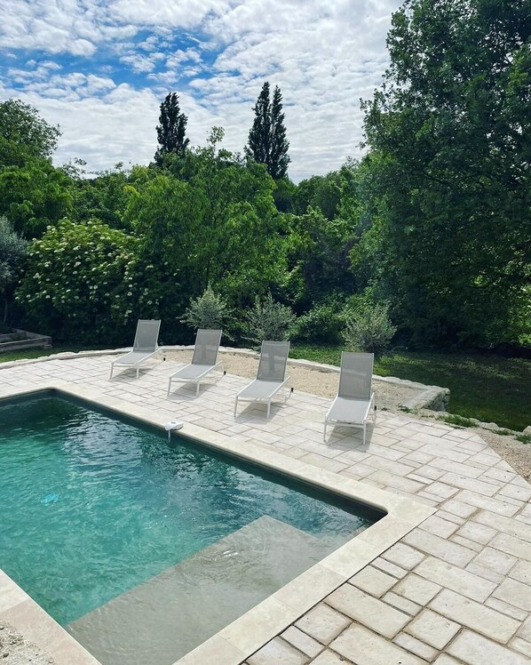 A rectangular swimming pool with a tiled deck and lounge chairs.