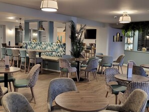 A modern restaurant interior with round tables, patterned chairs, and a central seating area with a patterned sofa. - Milford on Sea - 4 Bedroom Lodge (Downton)