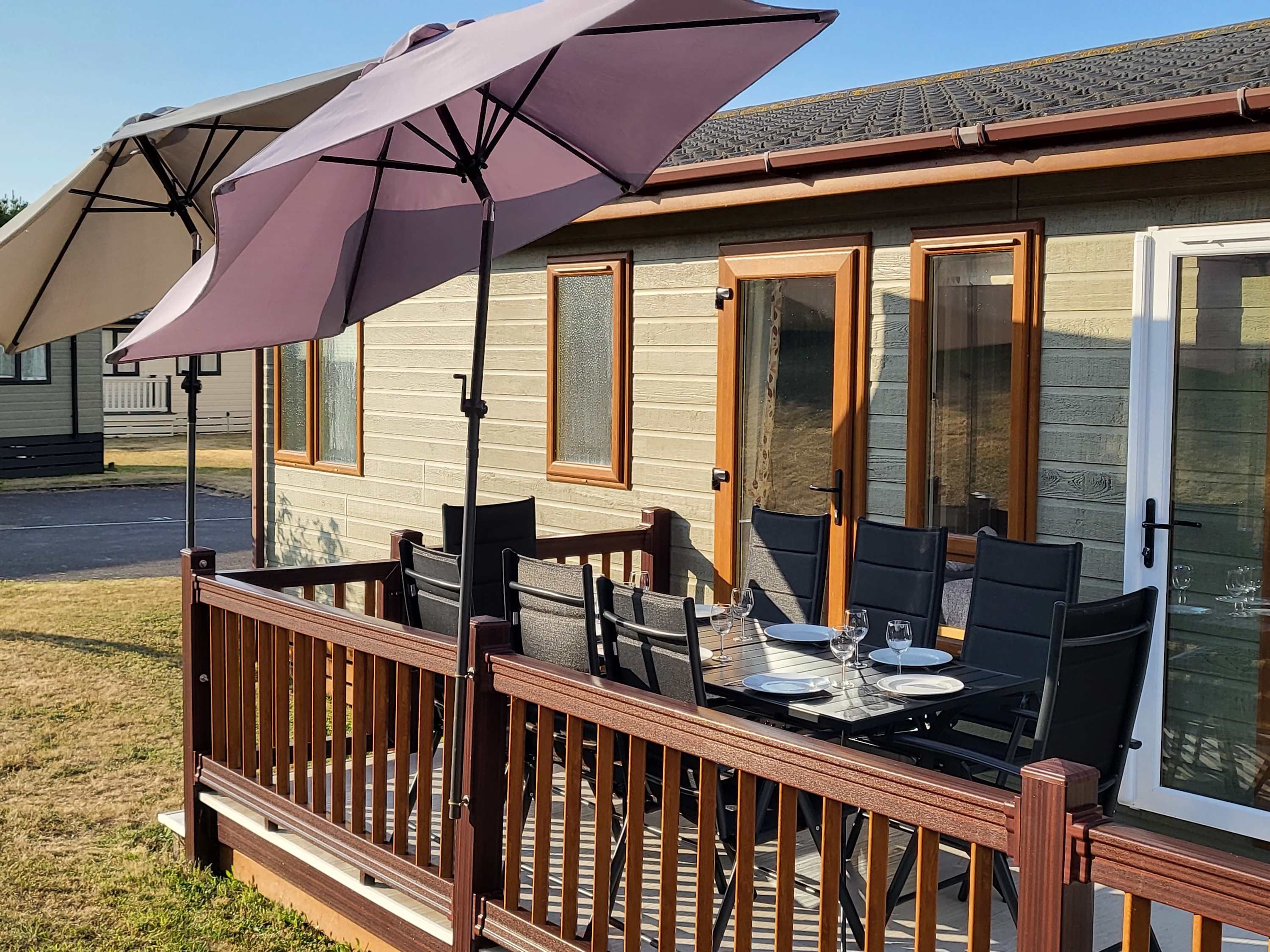 A deck with a table set for dining, a patio umbrella, and a house with wooden siding and glass doors.