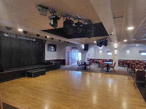 En rymlig inomhuslokal med en scen som är markerad med texten ”THE SHOWBAR” och med flera olika typer av sittplatser.
