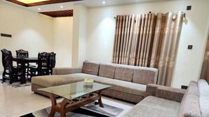 A living room with a sofa, a glass coffee table, a dining table with chairs, and a curtain.