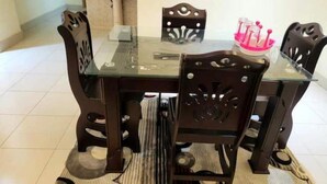 A dining table with a glass top and wooden chairs, a pink decorative item on the table, and a striped rug on the floor.