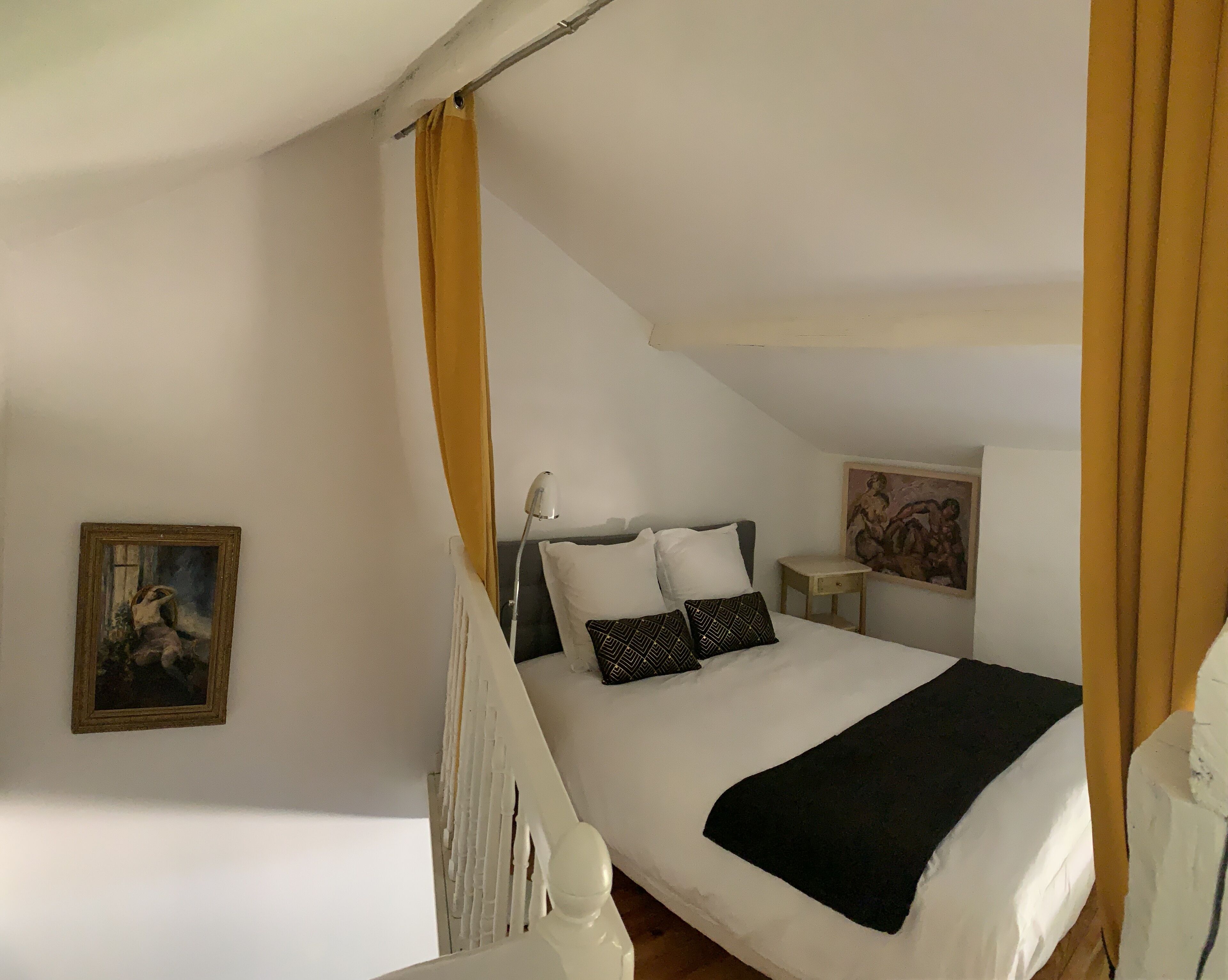 Ein Schlafzimmer mit einem Bett, einem Nachttisch, einer Lampe, einem Gemälde und einem Fenster mit Vorhängen.
