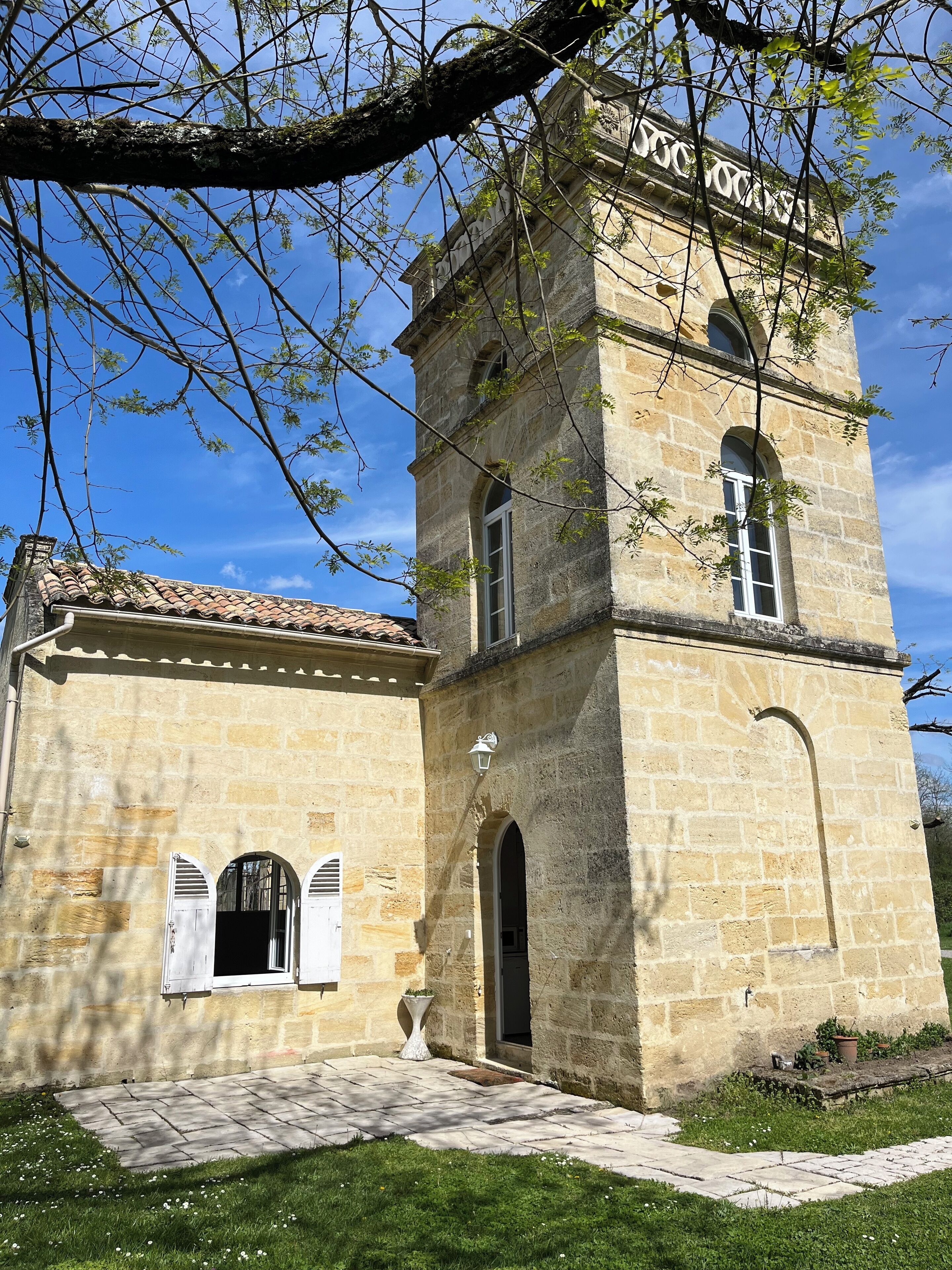 Un bâtiment en pierre avec un toit en tuiles, un clocher et un petit jardin.