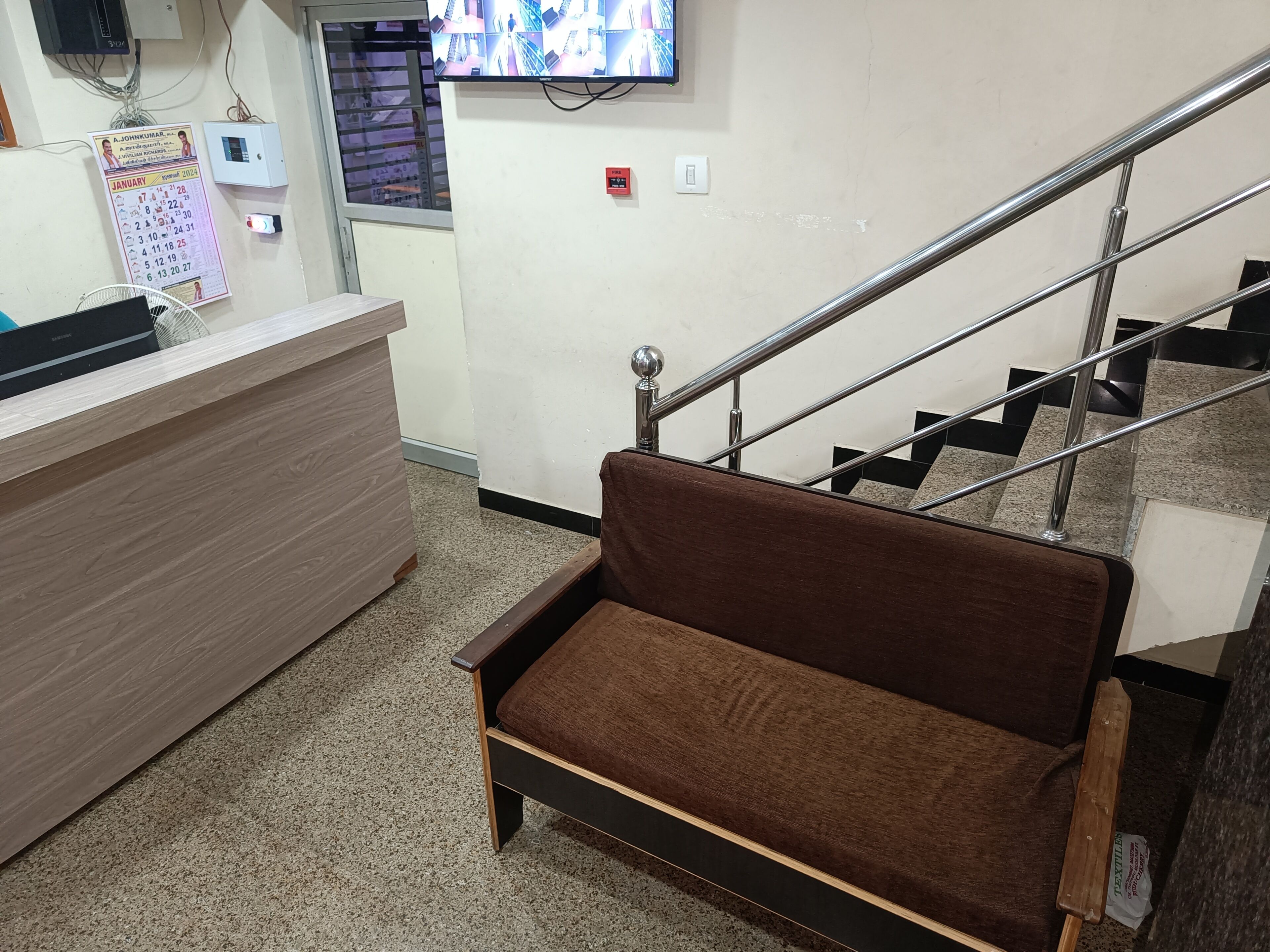 Un espace d’accueil comprenant un bureau en bois, un banc marron avec coussin, un détecteur d’incendie et un escalier avec des rampes en métal.