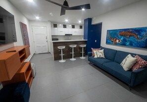 A modern living room with a blue sofa, a TV, and a kitchen area with white cabinets and stools. - Apartamento, en Marbella

 (Cartagena de Indias)