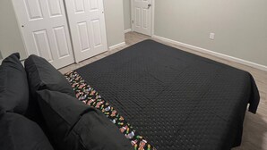 Une chambre avec un grand lit, deux portes blanches, un petit couloir et une bouche d’aération fixée au mur.