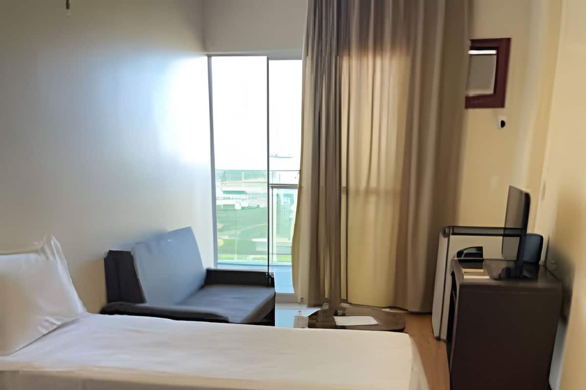 A hotel room with a bed, a sofa, a desk, and a window with curtains.