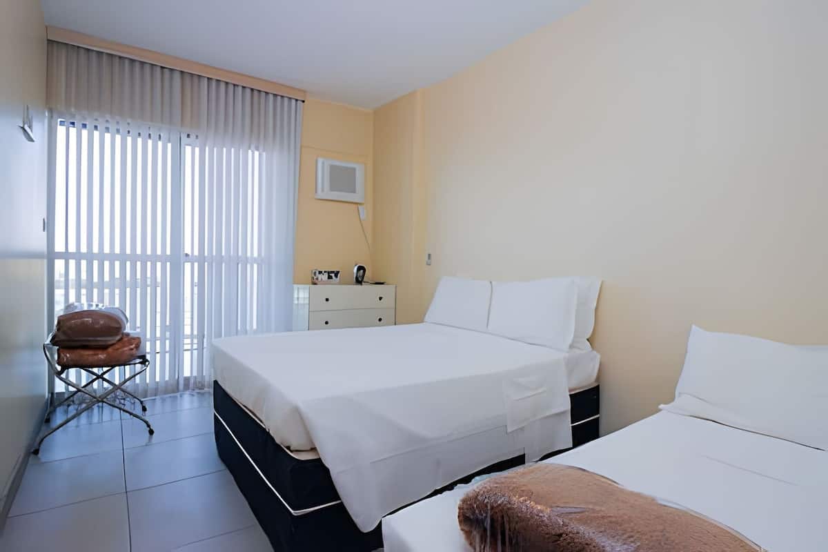A hotel room with two beds, a desk, a chair, and a window with blinds.