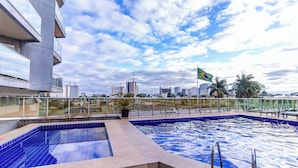 A rooftop pool with a cityscape view, a flag, and a modern building. - OZPED Flats Particulares Manhattan (Brasília)