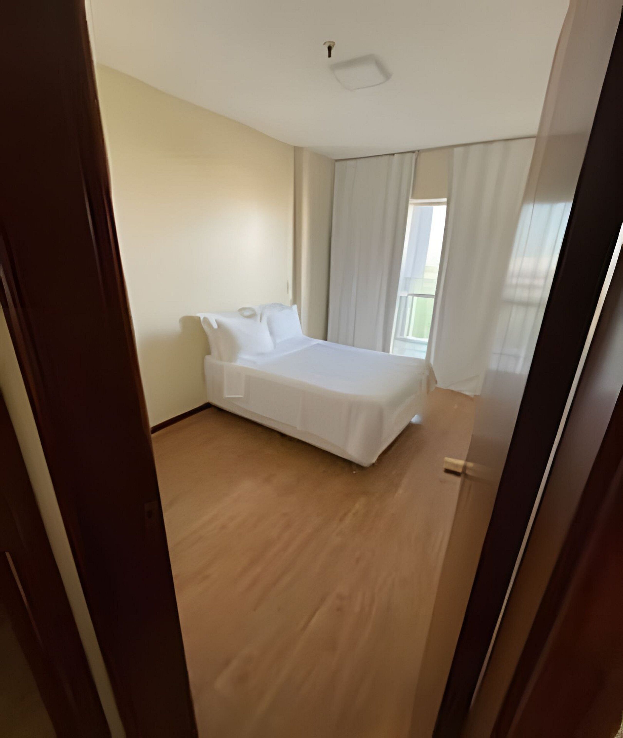 A bedroom with a bed, a window with curtains, and a wooden floor.