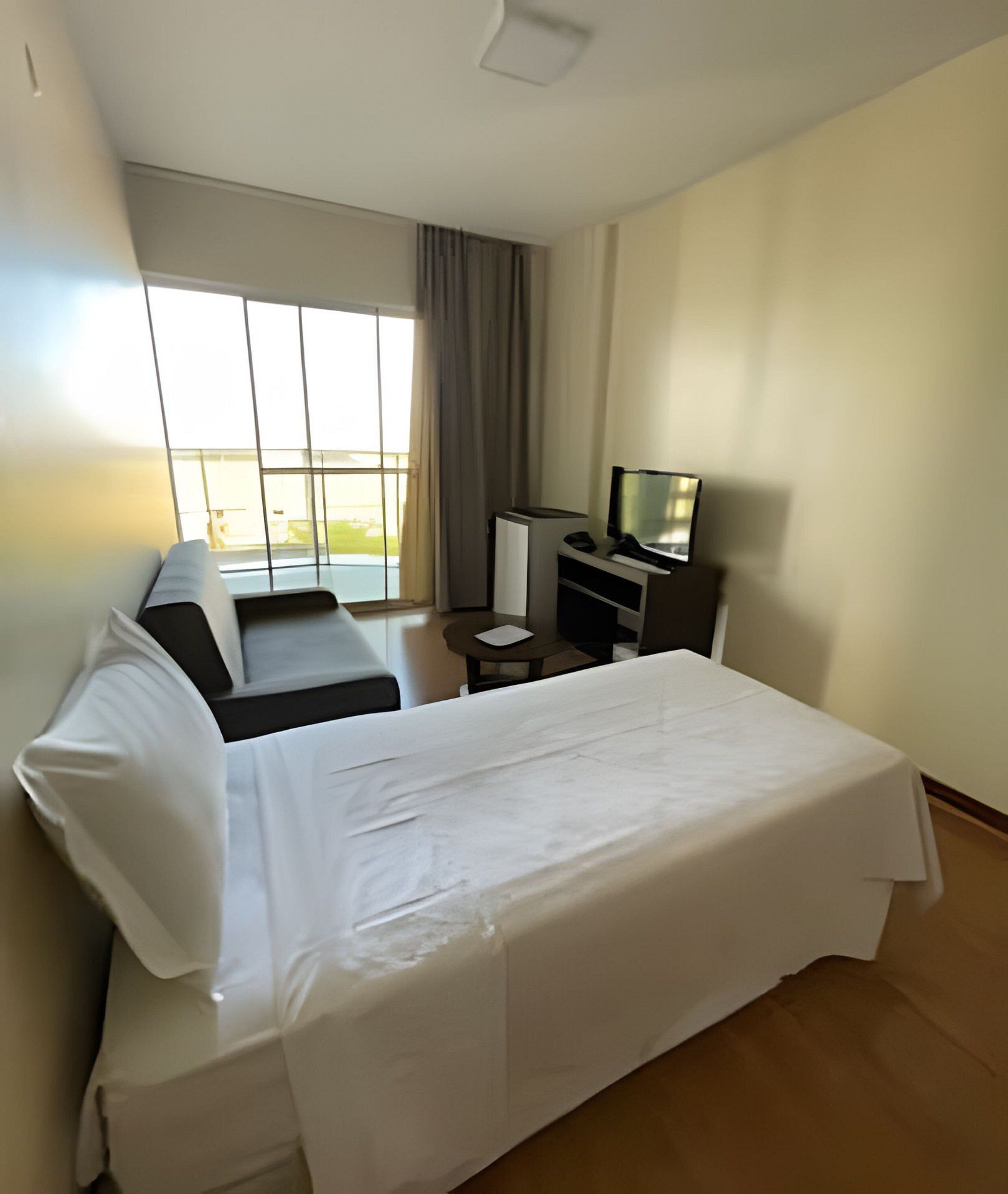Habitación de hotel con cama, sofá, escritorio, televisor y ventana con cortinas.