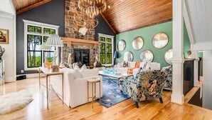 A spacious living room with a stone fireplace, wooden ceiling, and large windows. - Mountain Mansion 7BR, 10Ksf, Views, Pool, Sport Court, Gym, Sauna, Petting Zoo (Blue Ridge)