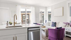 Una cocina moderna con lavavajillas, una encimera blanca y una zona de comedor con una silla morada.