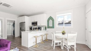Una cocina moderna con armarios blancos, una isla central, taburetes de bar y una mesa de comedor con sillas blancas.