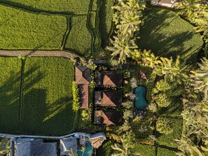 An aerial view of a property with a swimming pool, multiple buildings, and surrounding green fields.