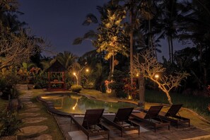 A nighttime outdoor pool area with lounge chairs, a gazebo, and palm trees.