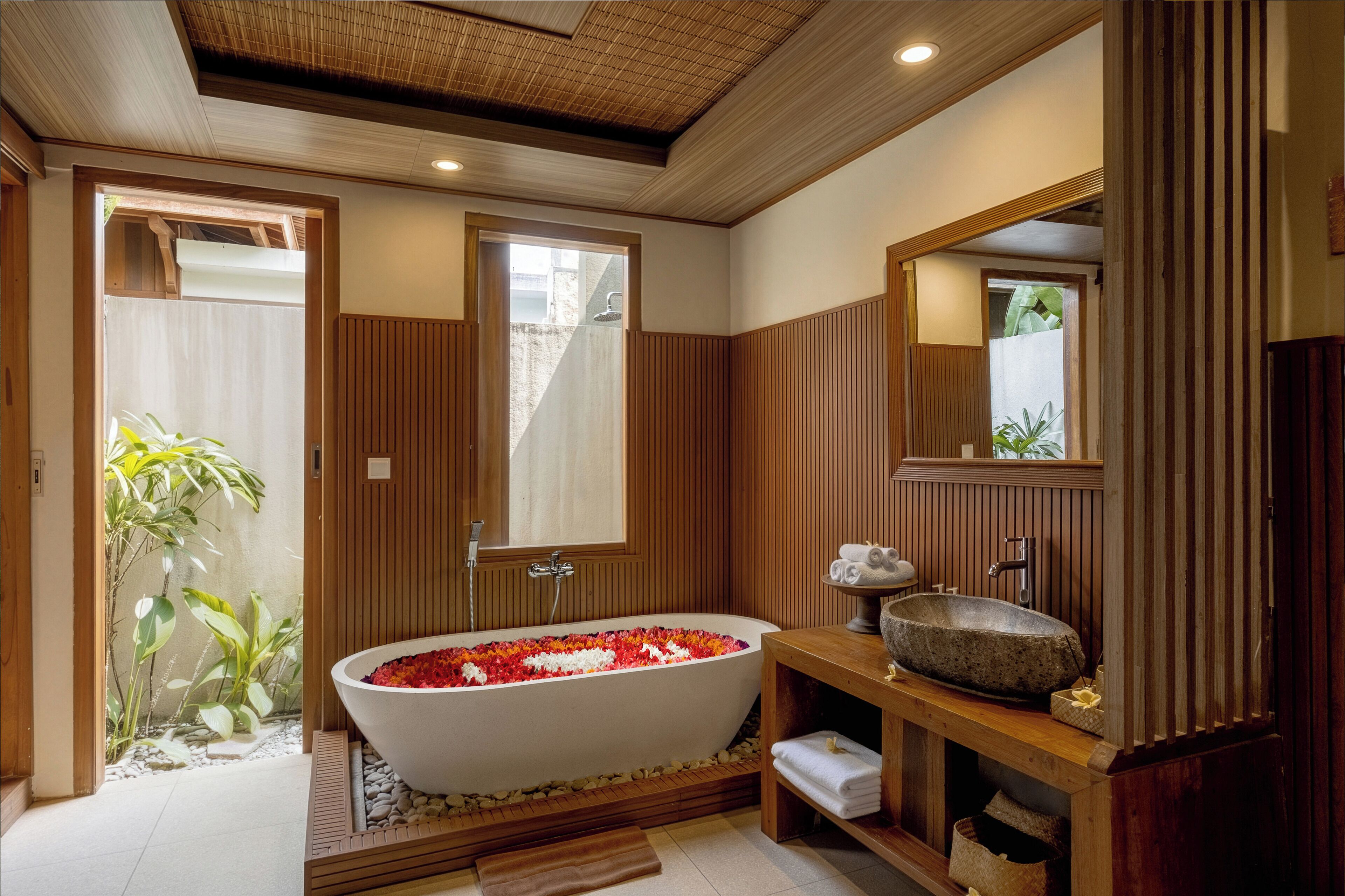 Un baño moderno con una bañera independiente, paneles de madera, un espejo grande y un lavabo pequeño.