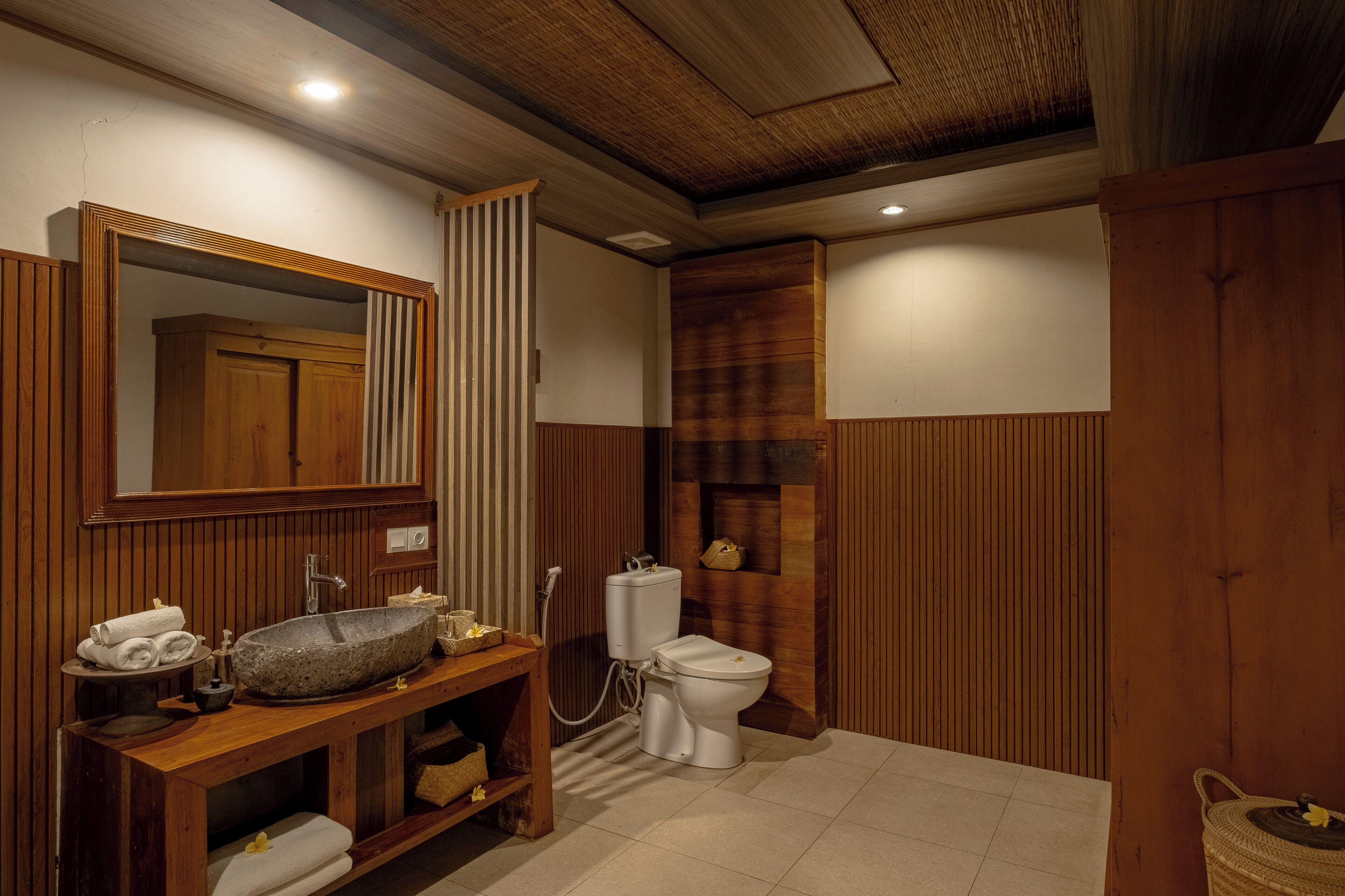 A bathroom with a wooden vanity, a stone sink, a toilet, and a mirror.