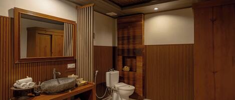 A bathroom with a wooden vanity, a stone sink, a toilet, and a mirror.