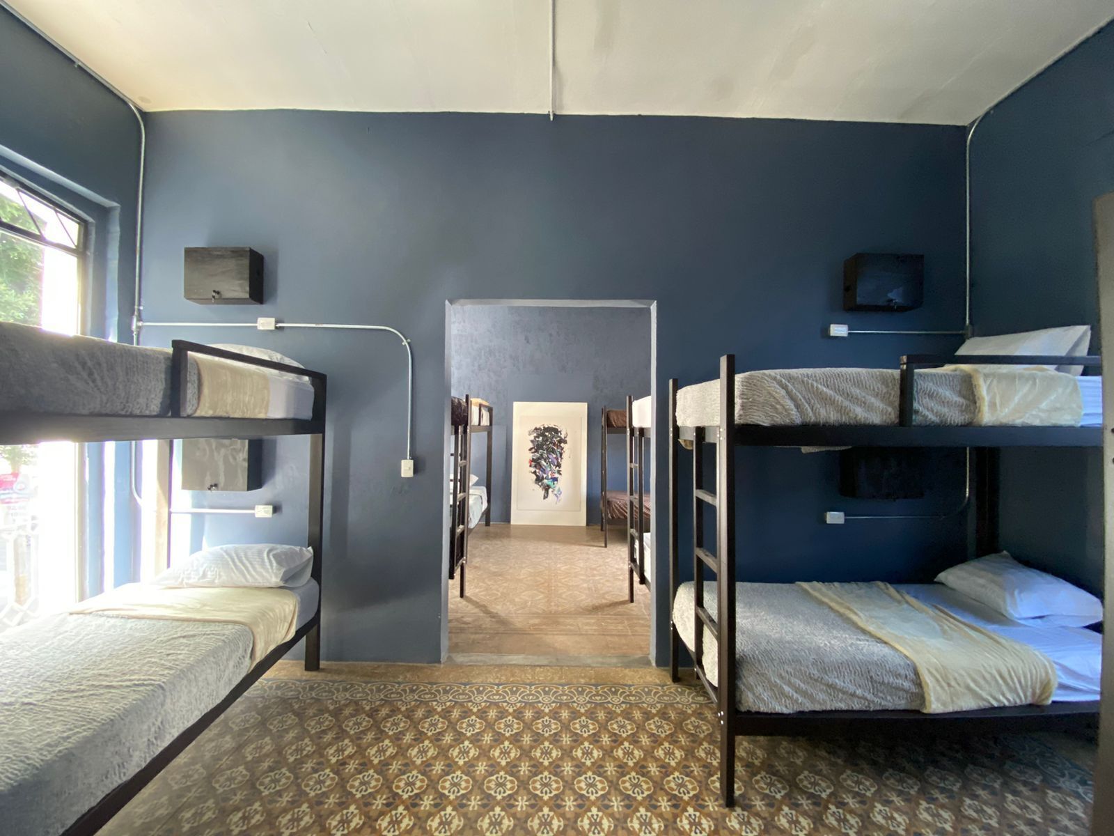A dormitory room with bunk beds, a patterned carpet, and a hallway leading to another room.