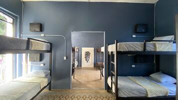 A dormitory room with bunk beds, a patterned carpet, and a hallway leading to another room.