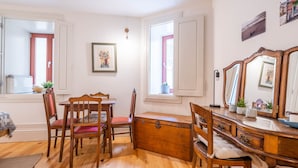A room with a wooden dining table, chairs, a dresser, and a mirror. There are windows with shutters and a framed picture on the wall. - Taipas Tranquility: Cozy T0 by LovelyStay (Porto)