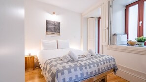 Et pænt opredt soveværelse med seng, et natbord med lampe, et vindue med udsigt og et billede på væggen.
