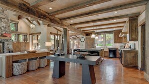 A spacious kitchen with wooden beams, a large island, and a stone fireplace.