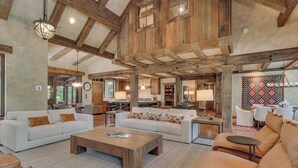 A spacious living area with a high ceiling, wooden beams, and a large window.
