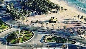 An aerial view of a coastal area with a beach, palm trees, and a road with a roundabout. - Mons Boutique Hotel and Apartment  (Da Nang)