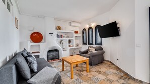 Un salon comprenant un canapé, une table basse, une cheminée, des étagères avec des livres et des objets de décoration, et un téléviseur fixé au mur.