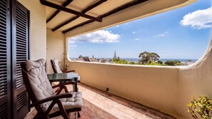 A balcony with a table and chairs, a view of the sea, and a building in the distance. - Downtown Carvoeiro 1BDR Apart W/View by LovelyStay (Praia do Carvoeiro)