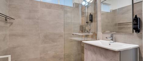 Un baño moderno con ducha, lavamanos y espejo.