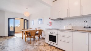 A modern kitchen with white cabinets, a built-in oven, and a dining area with a table and chairs.
