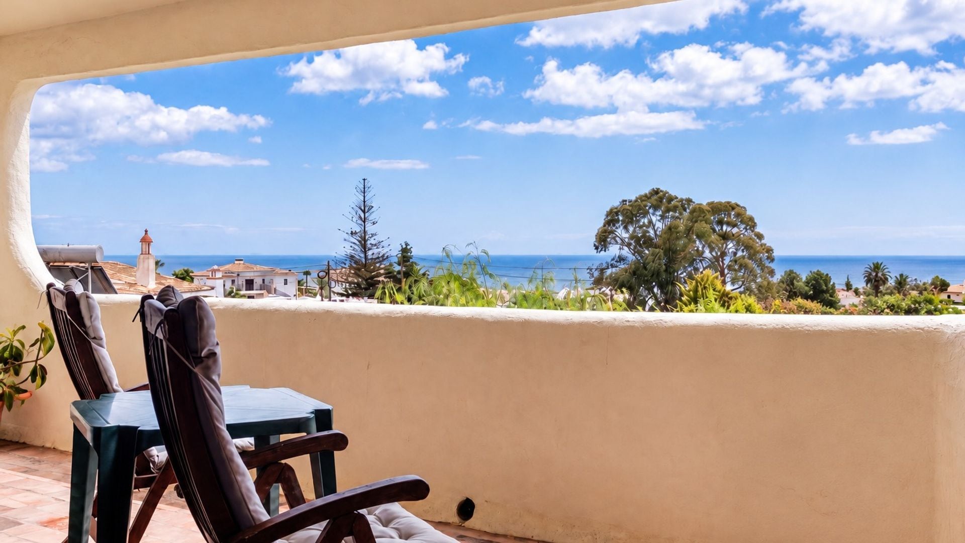 A balcony with a view of the sea, a table, and chairs.
