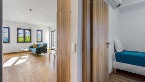 Una habitación moderna con piso de madera, sofá azul, una mesita y ventana con vista a zonas verdes.