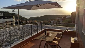 Una terraza con mesa y sillas, una sombrilla y vistas a un pueblo y colinas al fondo.