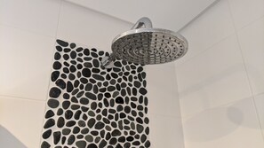 A shower with a perforated metal head and a wall with a pebble-like pattern. - Sesimbra 3BDR Apartment W/Terrace by LovelyStay (Castelo)